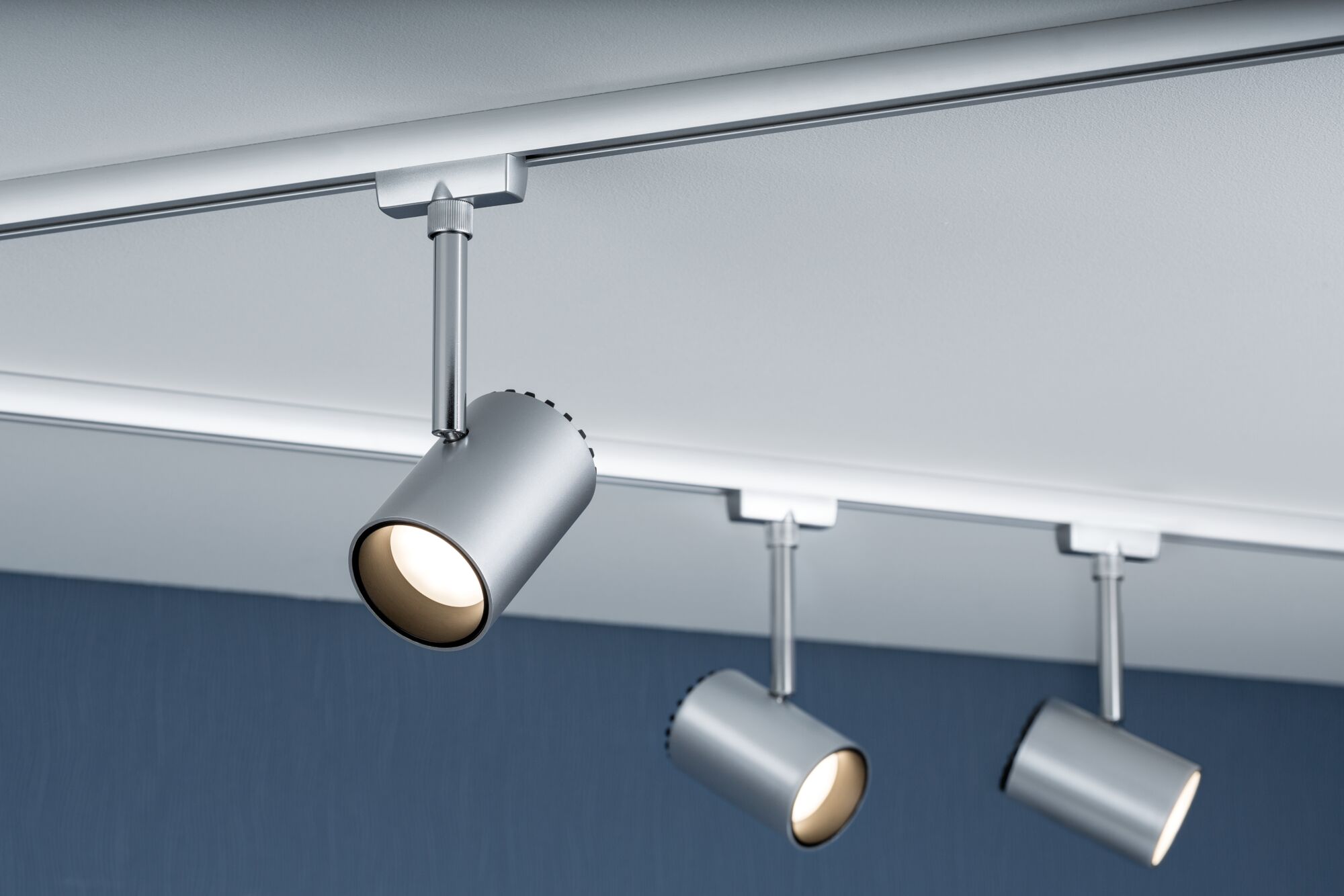 Trois spots LED métalliques argentés fixés sur rail blanc au plafond pour éclairage d'accent
