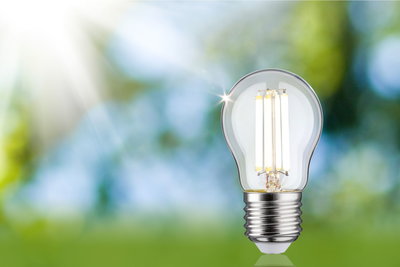 LED-pære med klart glas og sølvbase mod grøn-blå baggrund til energibesparende belysning