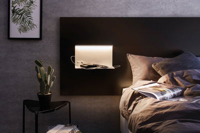 Moderne witte metalen wandlamp met plank aan donker hoofdeinde in slaapkamer.