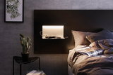 Moderne weiße Wandlampe aus Metall mit Ablagefläche an dunklem Kopfteil im Schlafzimmer.
