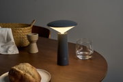 Modern black metal table lamp with warm white light on wooden table near glass and bread basket
