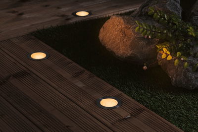 Round LED recessed lights with warm white glow in dark wooden terrace floor for outdoor lighting.