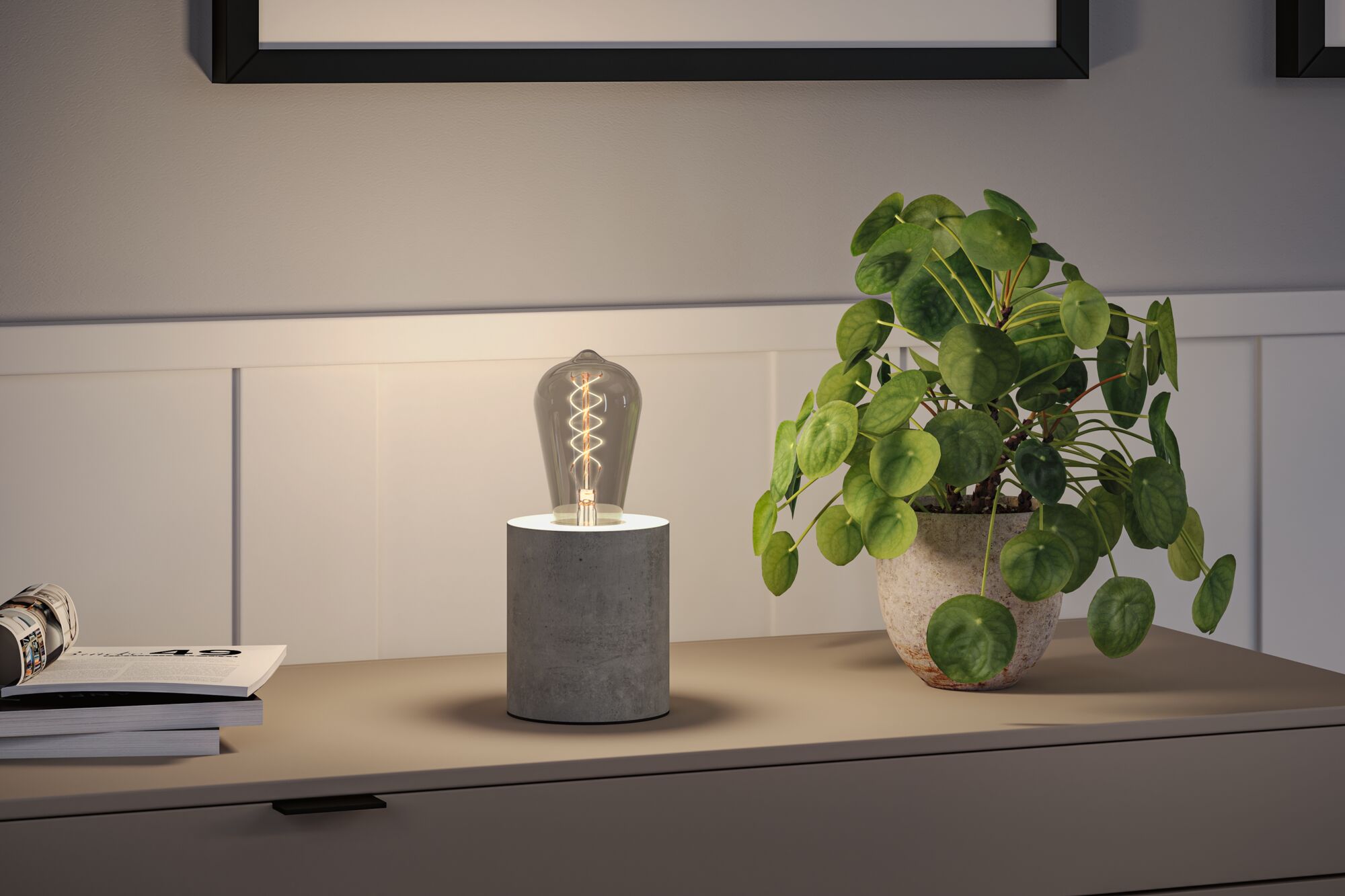 Modern table lamp with grey concrete base and decorative bulb on sideboard next to green houseplant