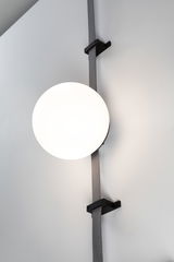 Modern wall lamp with round white glass and black mount on grey strap for living spaces