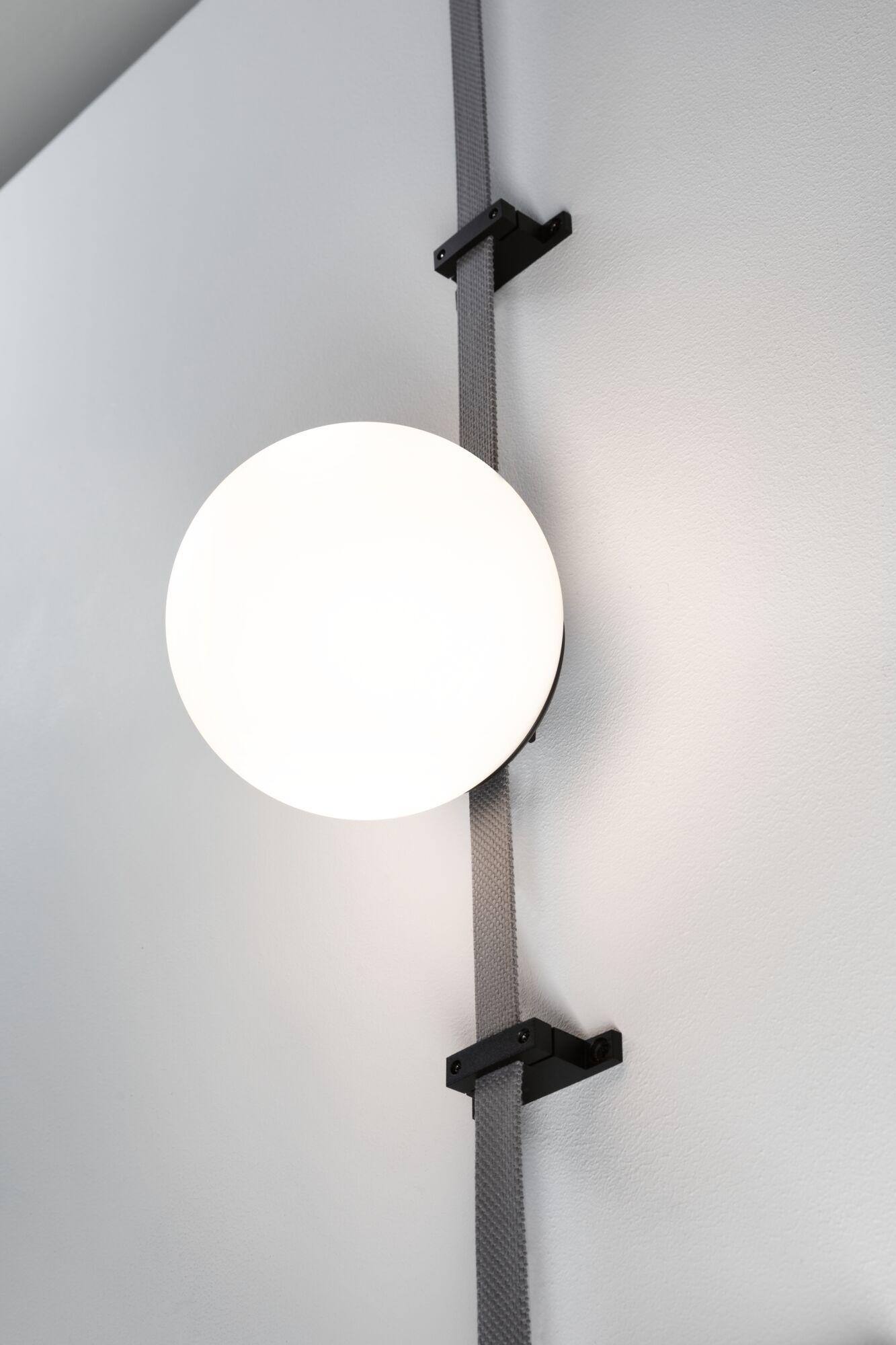 Moderne Wandlampe mit rundem weißem Glas und schwarzer Halterung an grauem Band für Wohnräume