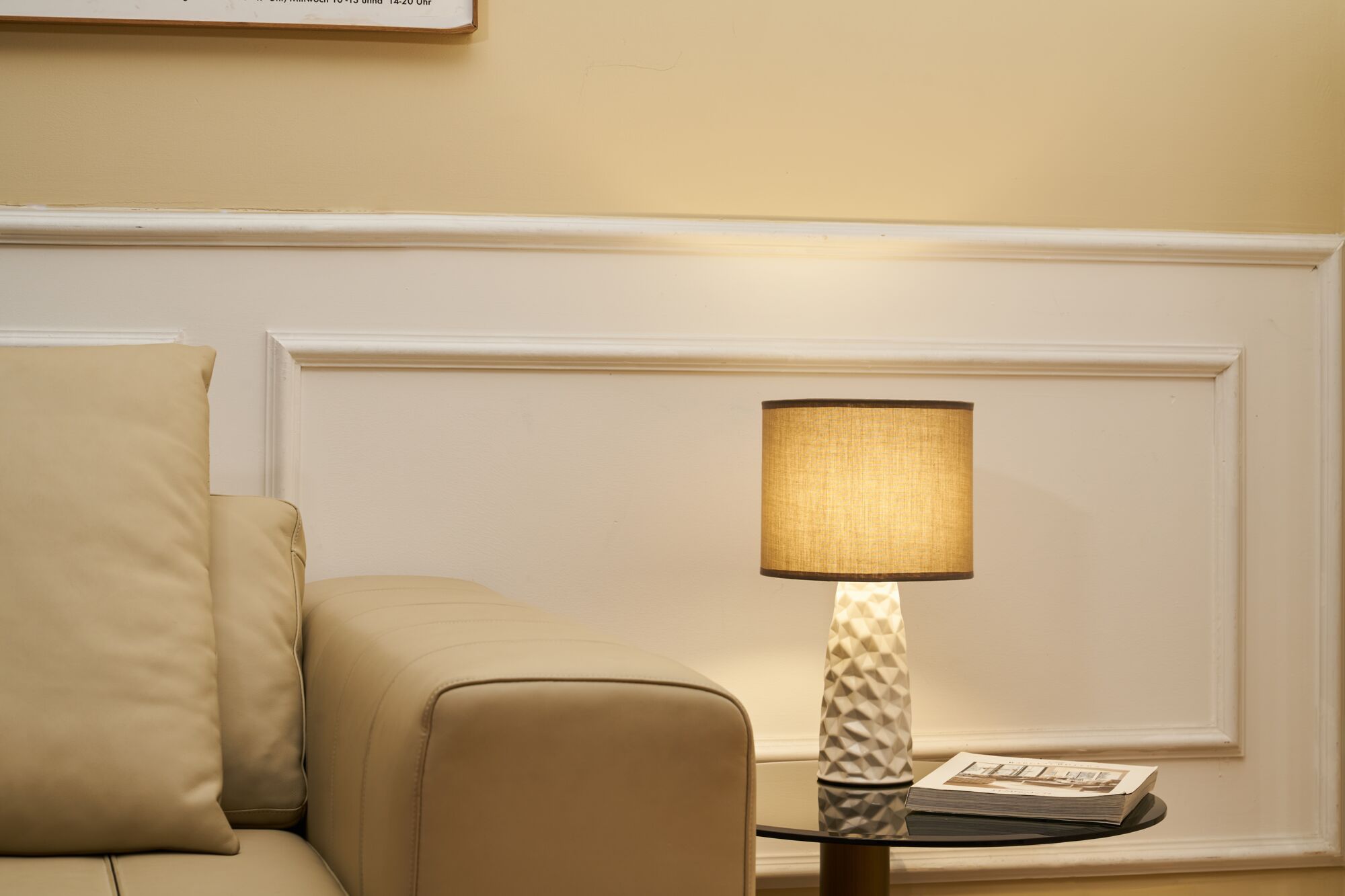 Beige leren bank naast zwarte glazen tafel met witte keramische lamp en beige lampenkap in woonkamer