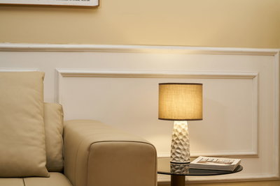 Beige lædersofa ved siden af sort glasbord med hvid keramisk lampe og beige lampeskærm i stue