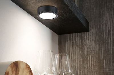 Round black metal LED ceiling light with warm white glow above glasses in modern kitchen