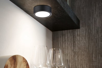 Runde schwarze LED-Deckenleuchte aus Metall mit warmweißem Licht über Gläsern in moderner Küche