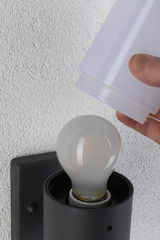 Hand setzt weißen Lampenschirm auf schwarze Wandlampe mit Glühbirne an weißer Wand montiert