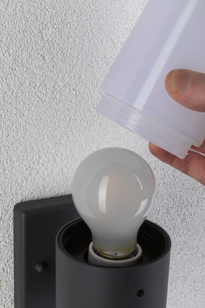 Hand setzt weißen Lampenschirm auf schwarze Wandlampe mit Glühbirne an weißer Wand montiert