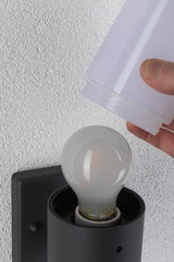 Hand placing white lampshade on black wall light with bulb mounted on white textured wall