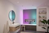 Modernes Badezimmer mit Holz-Waschtisch, runden Spiegel und farbiger LED-Deckenbeleuchtung für Wohnraum.