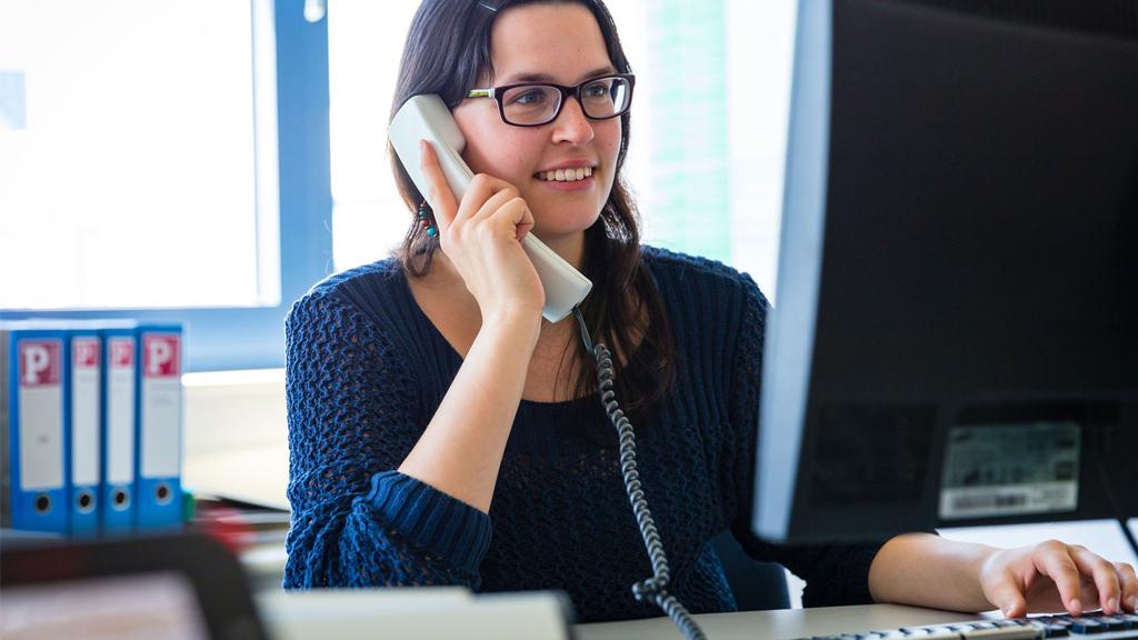 Woman with glasses on phone at desk in front of computer, representing customer service and support