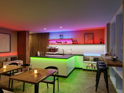 Bar moderne avec bandes LED vertes, rouges et bleues, mobilier en bois et coin salon confortable.