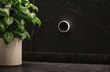 Round black wall dimmer with white edge on black marble wall next to green houseplant in white pot