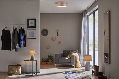 Moderner Wohnraum mit grauem Sessel, Holz-Deckenleuchte und zwei grauen Tischlampen für gemütliche Beleuchtung