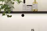 Black wall shelf with green plant and Meraki skincare products in white and yellow for bathroom decor