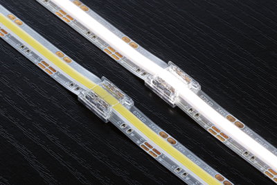 To hvide og gule LED-strips med klare stikforbindelser på sort træoverflade, LED-belysningstilbehør.