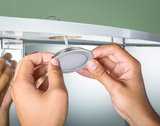 Hands installing round brushed aluminum LED recessed light in furniture with green wall background