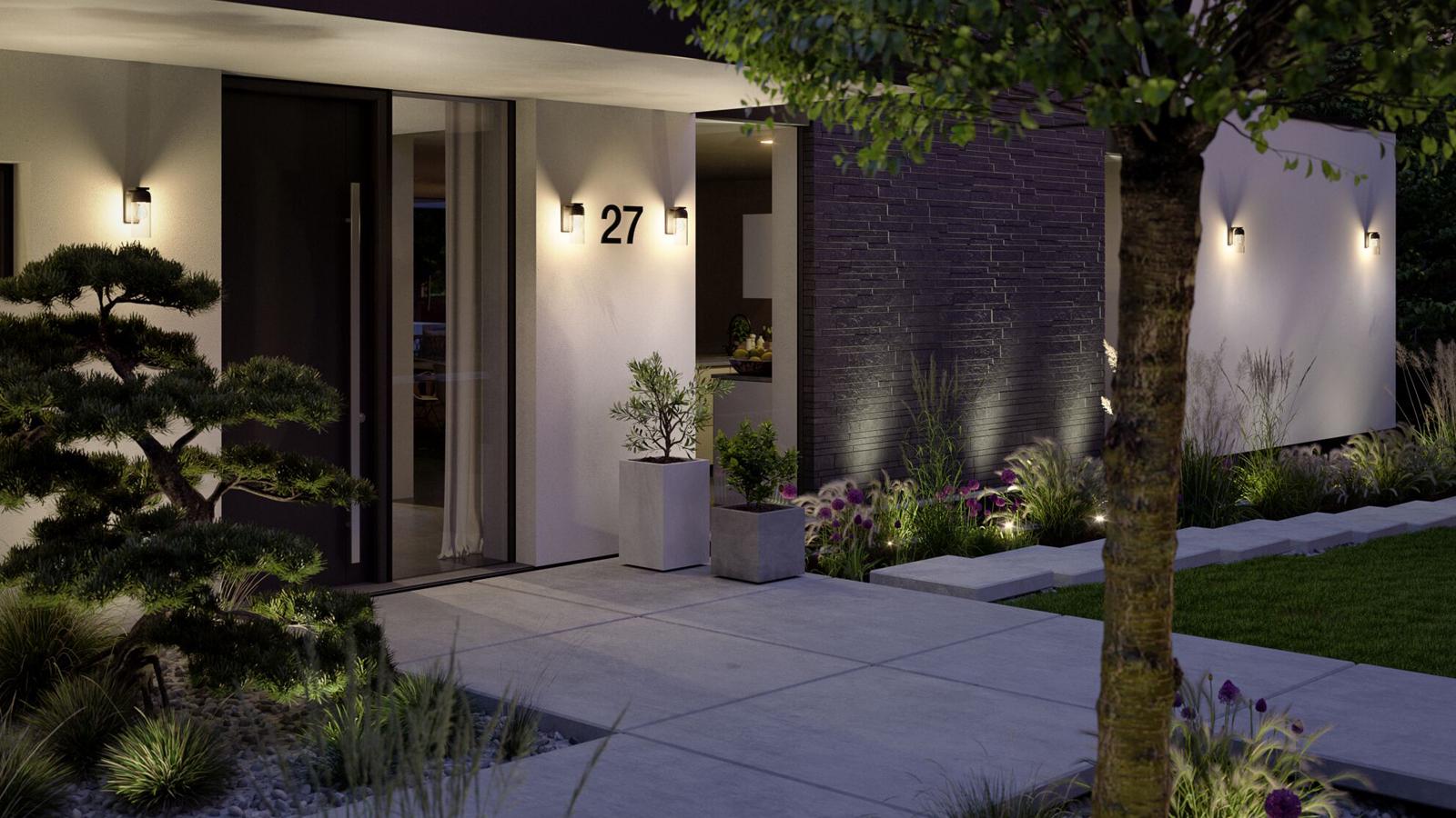 Moderne udendørsbelysning på hvidt hus med sort dør og havegang oplyst med planter og lys