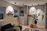 Salon moderne avec spots noirs au plafond, plantes et cadres décoratifs sur murs blancs.