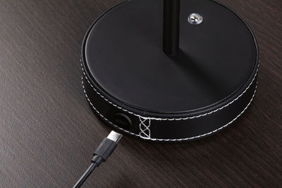 Black round lamp base with white stitching and USB-C charging cable on dark wood surface