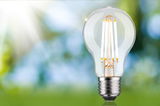 Classic LED light bulb with clear glass and silver base against green-blue blurred background