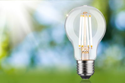 Classic LED light bulb with clear glass and silver base against green-blue blurred background