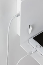 Weißes Ladekabel verbunden mit weißem Smartphone auf weißem Metallregal für moderne Elektronik.