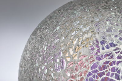 Close-up van een glazen mozaïekbol met transparante en paarse stukken voor decoratie.