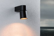 Black aluminum outdoor wall light with warm white glow on white wall, modern exterior lighting
