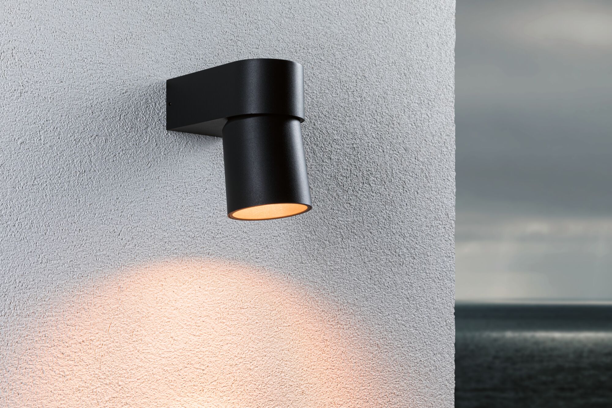 Black aluminum outdoor wall light with warm white glow on white wall, modern exterior lighting