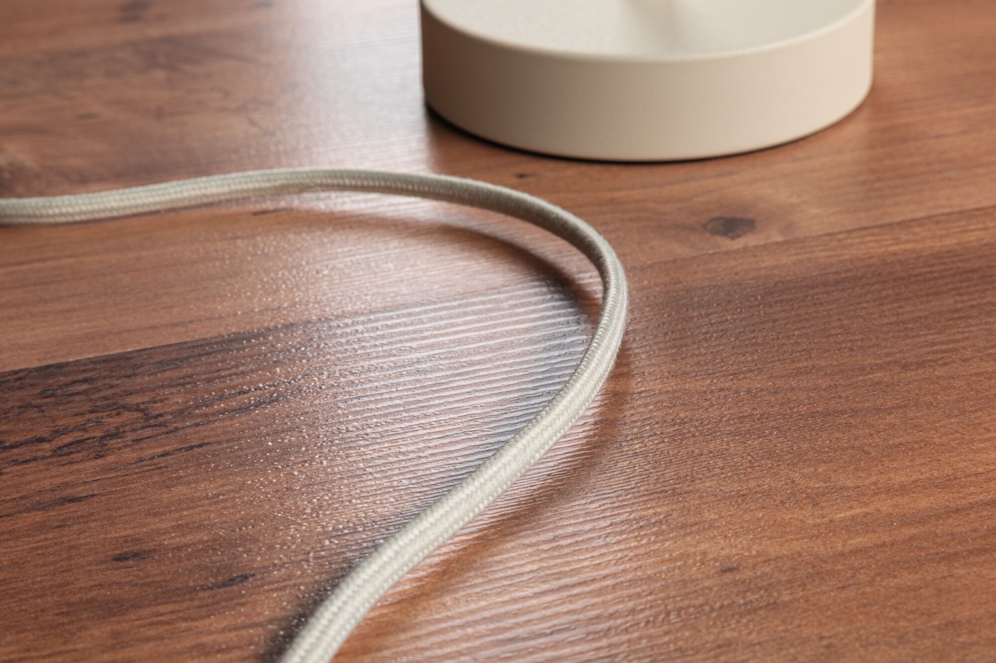Beige fabric cable on wooden surface with round cream lamp base, lighting accessory