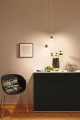 Commode noire moderne avec dessus blanc, décorée d’un vase, plante et sablier, éclairée par deux suspensions sphériques