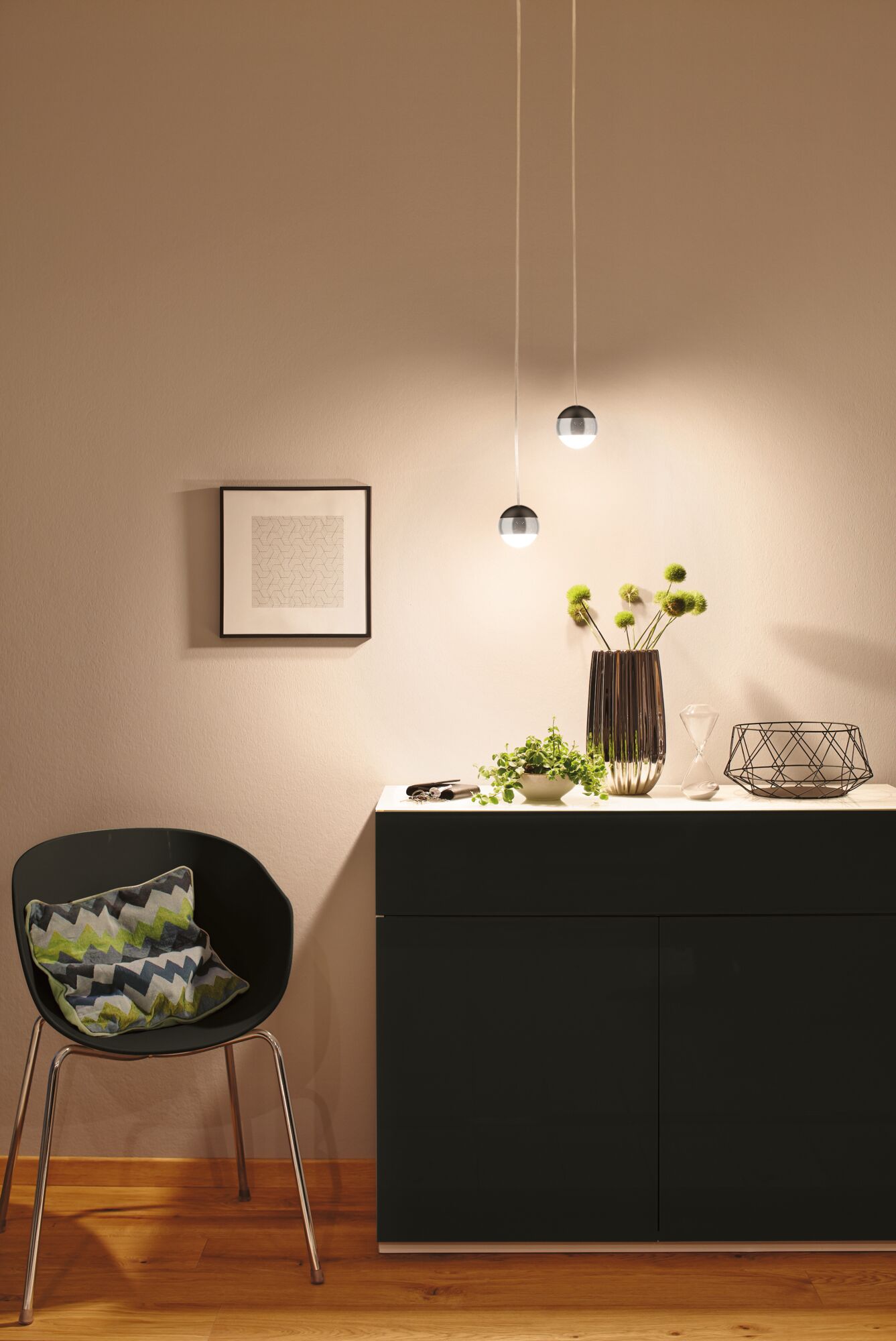 Modern black cabinet with white top, decorated with vase, plant, and hourglass, lit by two spherical pendant lights