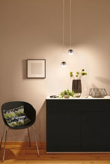 Modern black cabinet with white top, decorated with vase, plant, and hourglass, lit by two spherical pendant lights