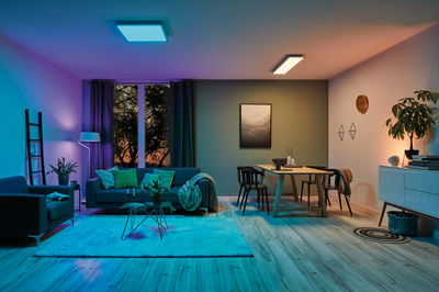 Moderne woonkamer met paarse en warmwitte LED-plafondlampen, bank en houten eettafel