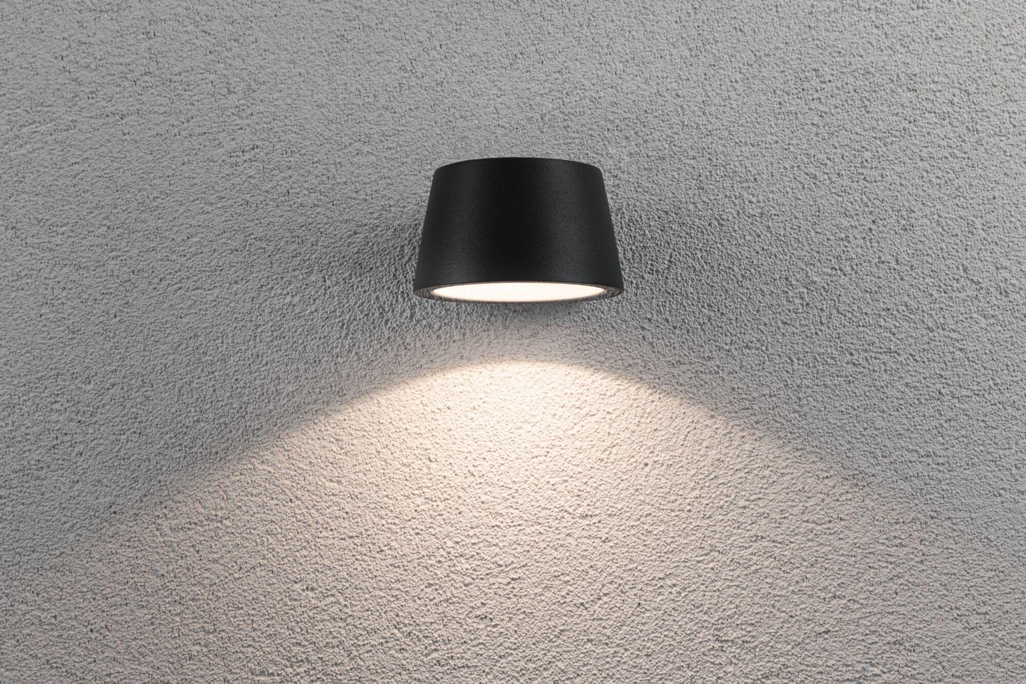 Schwarze Wandlampe aus Metall mit nach unten gerichtetem Licht auf grauer Strukturwand für Innenbeleuchtung