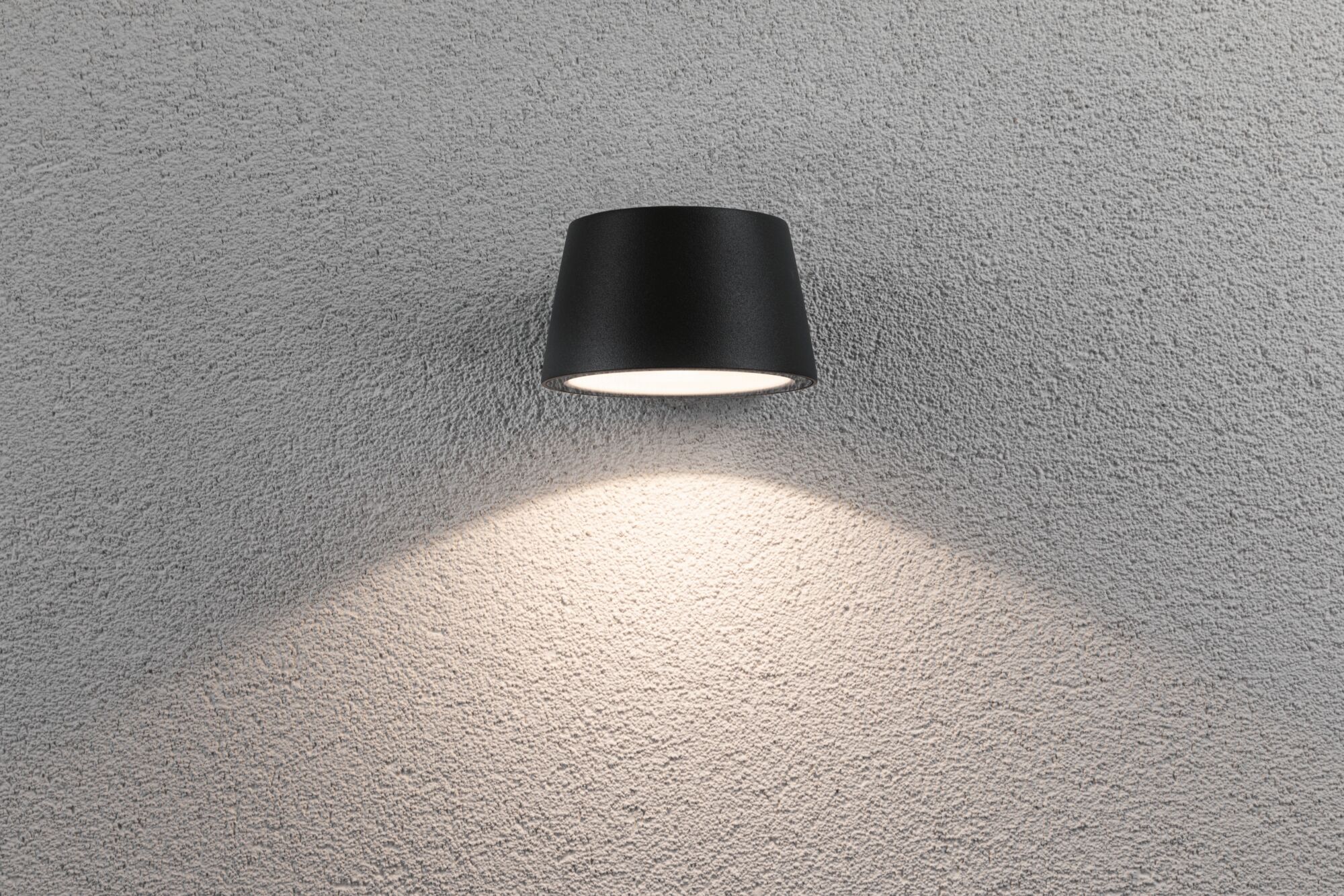 Schwarze Wandlampe aus Metall mit nach unten gerichtetem Licht auf grauer Strukturwand für Innenbeleuchtung