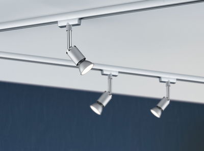 Trois spots LED métalliques argentés sur rail devant plafond blanc et fond bleu