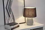 Modern table lamp with black and white striped ceramic base and black fabric shade on white table.