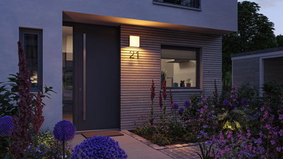 Moderne Hausfassade mit grauer Tür, Holzverkleidung und warmweißem Außenwandleuchter bei Abendlicht