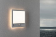 Square white LED wall light with motion sensor on grey exterior wall overlooking the sea