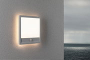 Square white LED wall light with motion sensor on grey exterior wall overlooking the sea