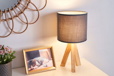 Lampe de table avec abat-jour en tissu marron et pied en bois tripode sur table claire près d'un cadre photo.