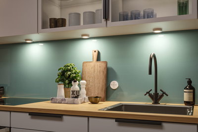 Plan de travail de cuisine moderne en bois avec évier en acier inoxydable et éclairage LED sous les meubles.