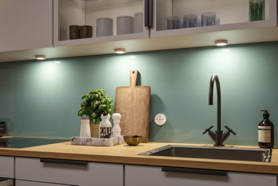 Plan de travail de cuisine moderne en bois avec évier en acier inoxydable et éclairage LED sous les meubles.