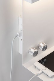 White metal shelf with two silver knobs and a white smartphone connected to a charging cable