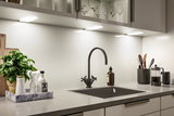 Modern kitchen countertop with black sink, matte black faucet, and LED under-cabinet lighting.